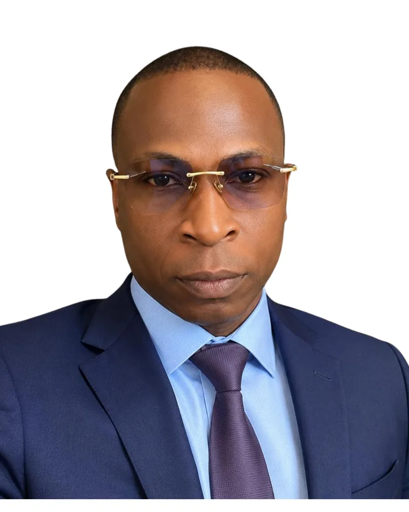 Portrait of a person wearing a navy suit, light blue shirt, purple tie and rimless glasses
