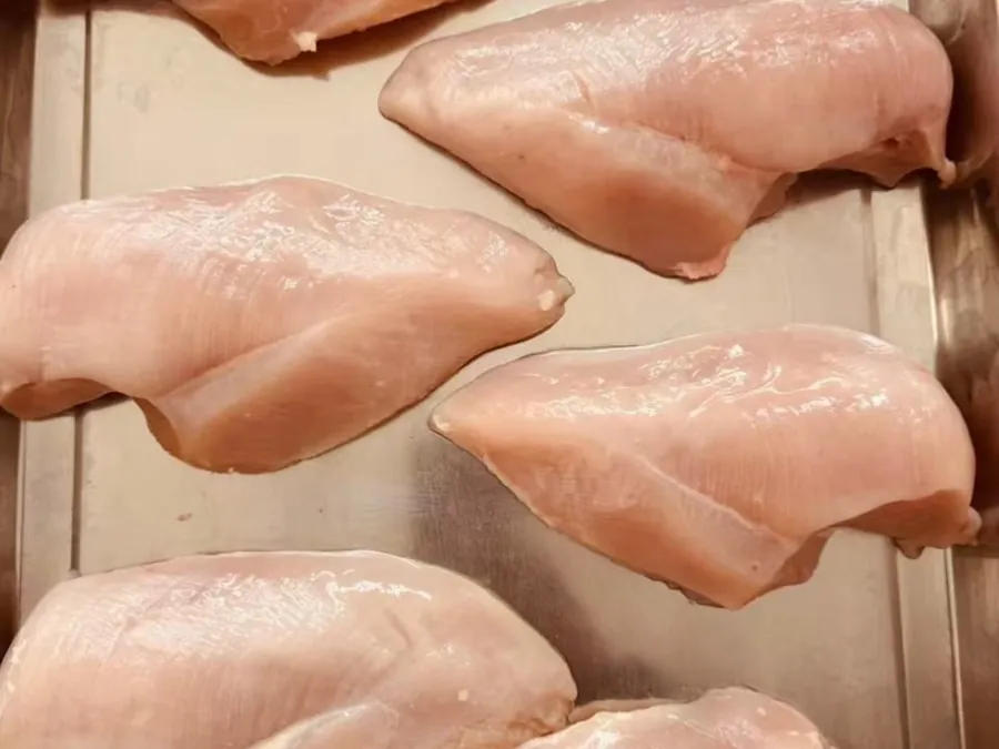 Six raw boneless chicken breast fillets on a stainless steel tray