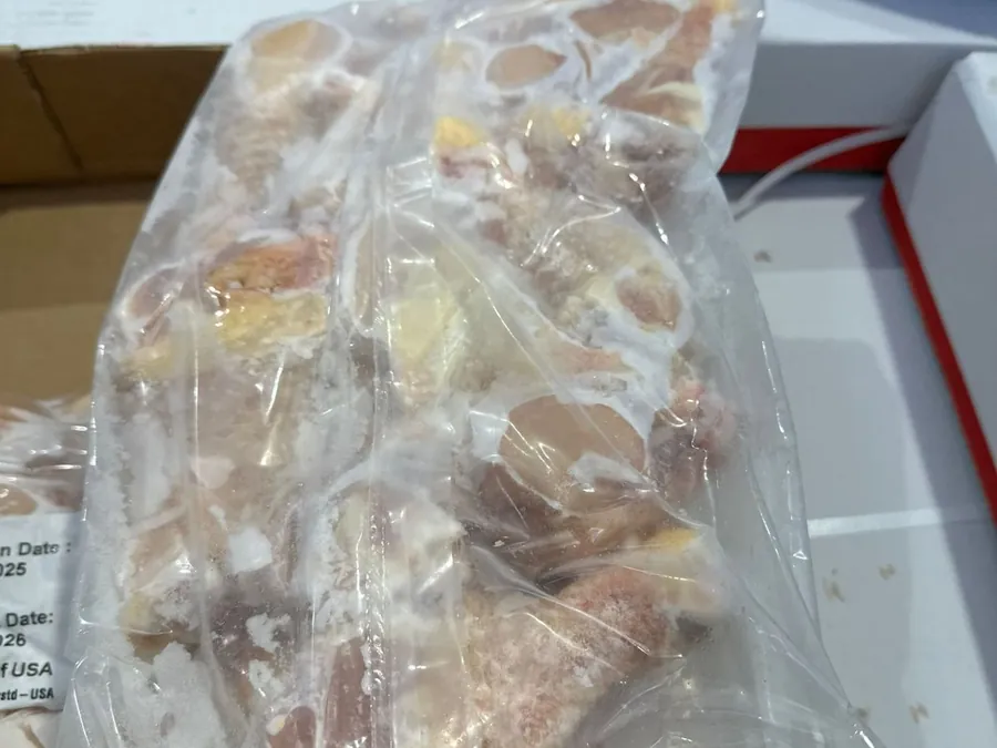 Sealed bag of frozen chicken pieces resting on stacked shipping cases