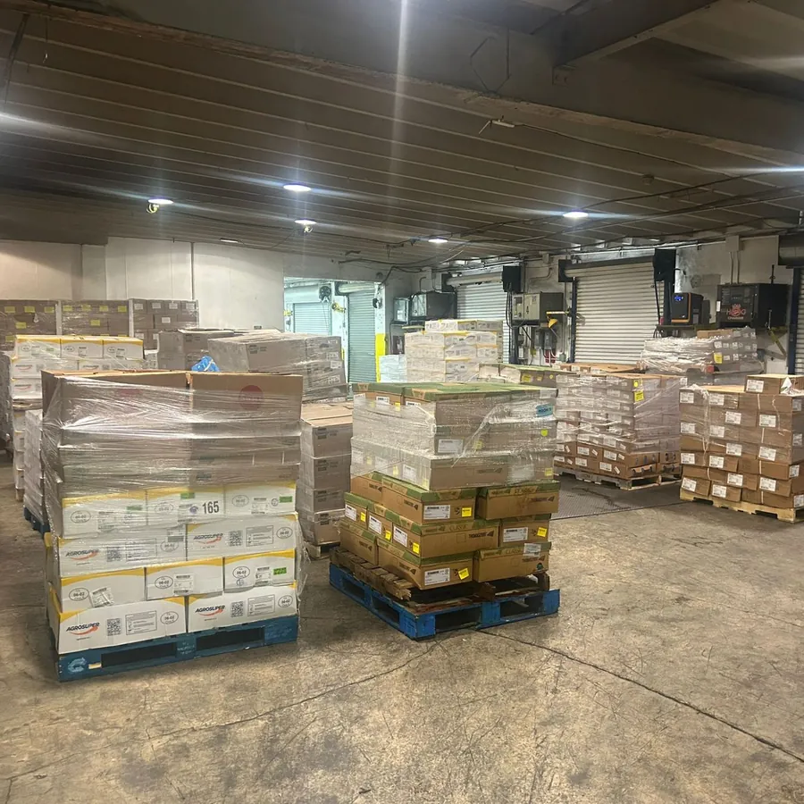 Warehouse floor with shrink-wrapped pallets of boxed product in front of roll-up loading dock doors