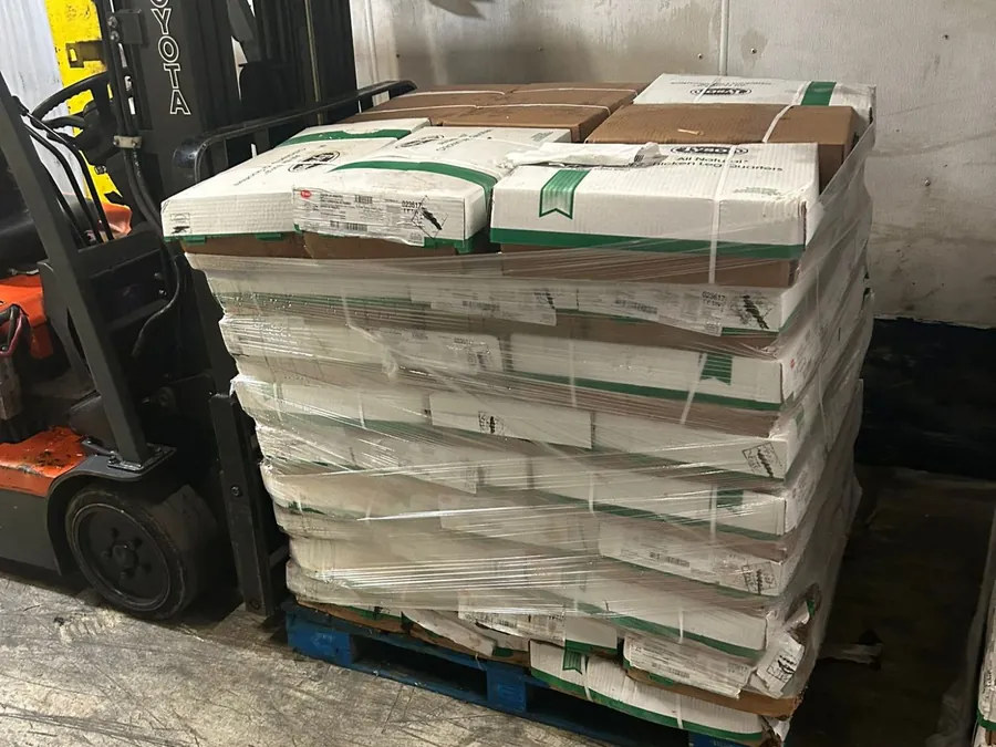 Shrink-wrapped pallet of stacked cases on a blue pallet beside a forklift