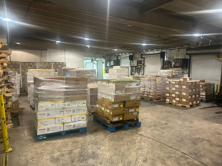 Shrink-wrapped pallets of boxed product on a warehouse floor in front of roll-up loading dock doors