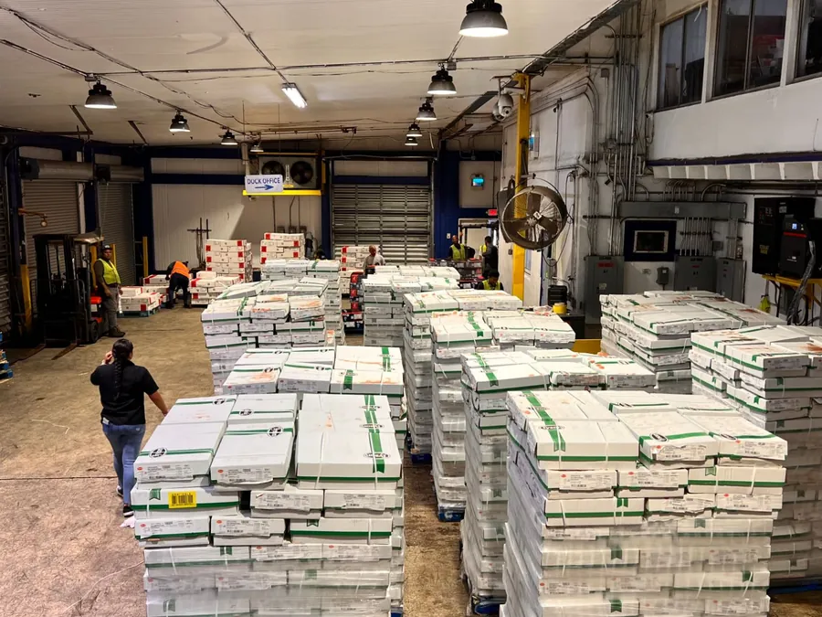 Team members and a forklift working among rows of palletized, shrink-wrapped cases near the dock office
