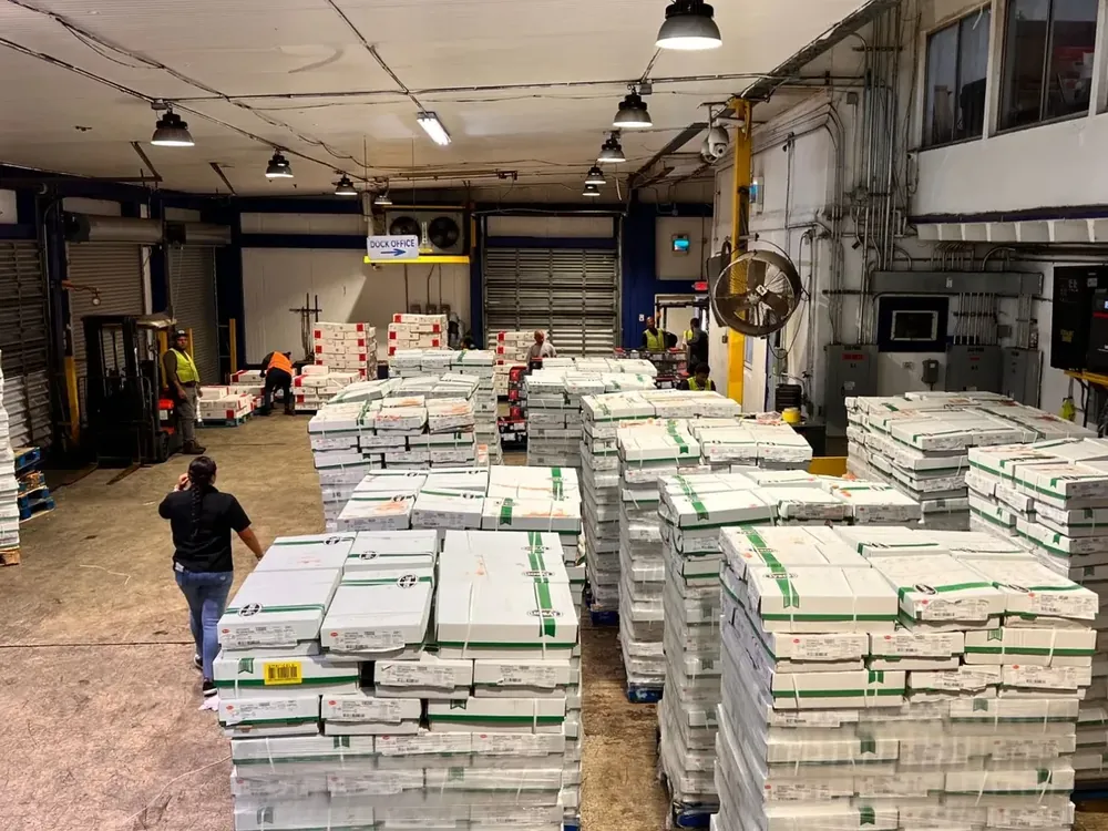 Team members and a forklift working among rows of palletized, shrink-wrapped cases near the dock office